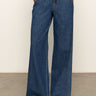 A person models Sanctuary Clothing's arden wide leg jeans in the shade perfect storm, standing with hands in pockets and paired with brown sandals against a plain background.