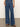 A person wears Sanctuary Clothing’s arden wide leg jeans in Perfect Storm, paired with brown sandals, standing on a concrete floor with hands in their front pockets.