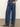 A person stands with hands in pockets, wearing Sanctuary Clothing’s arden wide leg jeans perfect storm and brown flat sandals against a plain light background.