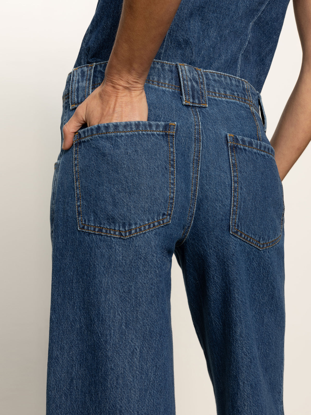 Close-up of a person wearing Sanctuary Clothing’s arden wide leg jeans perfect storm, shown from the back with one hand in the right back pocket. The jeans have visible stitching and two back pockets.