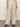 A figure in Sanctuary Clothing's hopper straight leg flax trousers and a sleeveless top stands on concrete. The outfit is light beige with dark sandals, and their head is not visible.