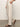 A person is wearing Sanctuary Clothing's hopper straight leg flax pants with hands in pockets, a tucked-in beige shirt, and brown sandals, standing on a smooth floor against a plain light wall.