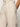 A close-up shows a person wearing Sanctuary Clothing's "hopper straight leg flax" trousers. They feature buttoned, high-waisted light beige fabric that looks textured and lightweight, like linen. One hand rests casually in a pocket.