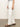 Someone stands sideways, wearing Sanctuary Clothing's hopper straight leg cargo pants in bleached white and brown sandals. A large pocket is visible on the thigh, and their hand rests by their side against a plain, neutral-toned background.