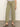 A person wearing Sanctuary Clothing's district column ankle jean bamboo—high-waisted, olive green wide-leg jeans with front patch pockets—paired with a white top and black heeled sandals, stands on a gray floor against a light background.