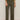 A person wearing Sanctuary Clothing's boyfriend utility pant kalamata and a green sweater with rolled-up sleeves, styled with black pointed-toe slingback shoes, stands against a plain light background.