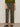 A person wearing Sanctuary Clothing's boyfriend utility pant kalamata and a green sweater with rolled-up sleeves, styled with black pointed-toe slingback shoes, stands against a plain light background.