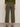A person wearing Sanctuary Clothing's boyfriend utility pant in kalamata with large back pockets and a green sweater stands on a grey floor facing away, paired with black sandals.