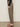 A person stands sideways in Sanctuary Clothing's boyfriend utility high rise pant in French Kitty, paired with a black long-sleeve top and black heeled sandals, against a neutral background.