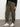 Someone wearing Sanctuary Clothing's sahara tapered pant in burnt olive from the inclusive collection, a black long-sleeve top, and white Veja sneakers stands on a gray floor against a plain white wall.