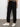 Wearing Sanctuary Clothing's sahara tapered pant in black, a person stands against a plain, light background. The image is cropped at the chest, highlighting only the lower half of their body.