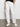 A person models the Sanctuary Clothing sahara tapered pant in chalk, standing with hands in pockets against a light wall and gray floor. The focus is on the lower half, styled with a black shirt and white sneakers.