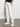 A person wearing Sanctuary Clothing's sahara tapered pant in chalk stands with one hand in their pocket against a plain gray floor and white wall, only the lower half of the body is visible.