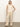 A woman stands against a plain background wearing Sanctuary Clothing's coastal pant sand sequin stripe—loose, beige, wide-leg pants with subtle shimmer—a sleeveless white knit top, black open-toe heels, and has straight light brown hair.