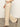 A person wearing Sanctuary Clothing’s coastal pant sand sequin stripe and black heeled sandals walks indoors on a polished floor, one hand in their pocket. The image is cropped above the waist.