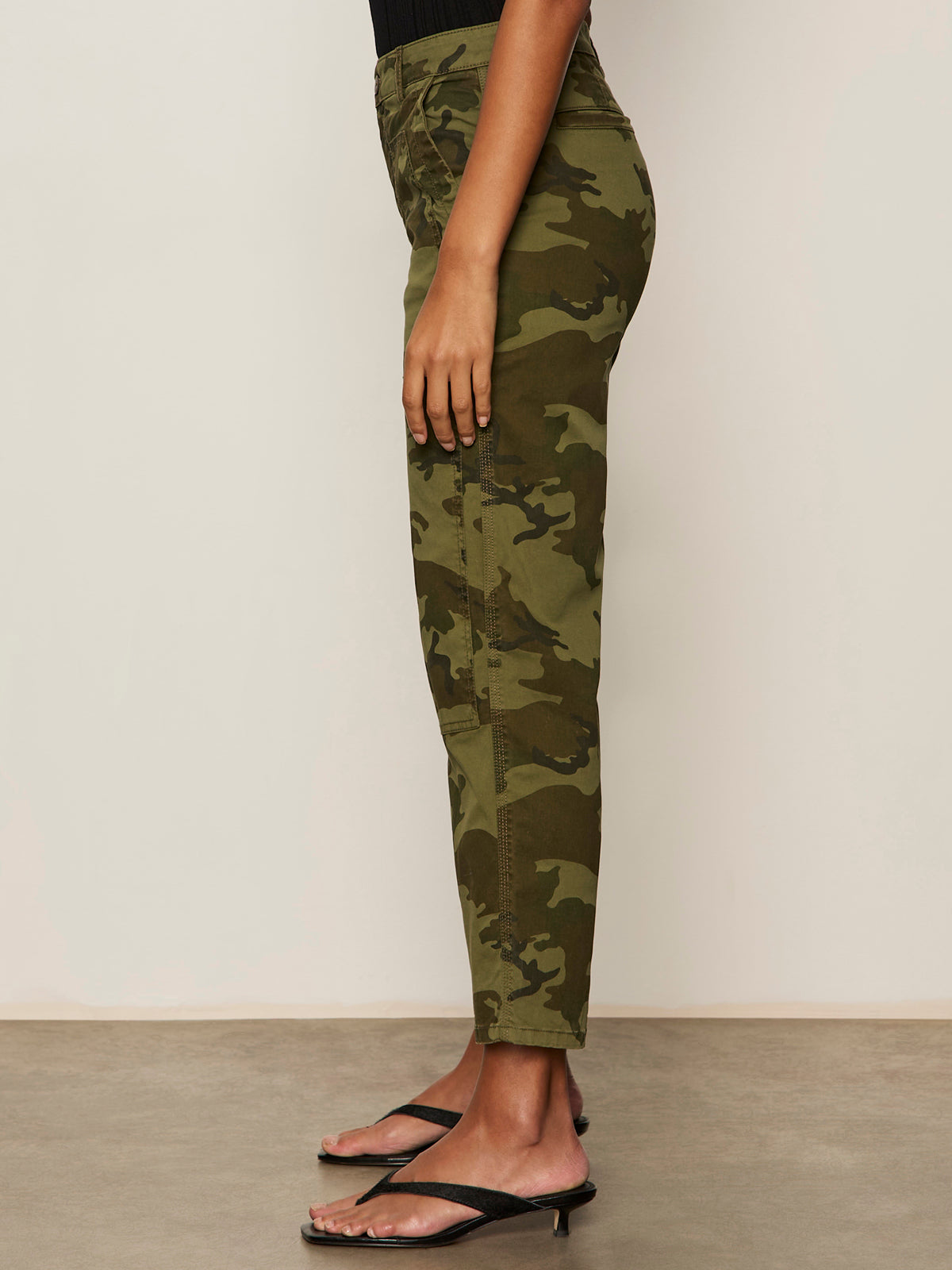 A person stands sideways against a plain background wearing Sanctuary Clothing’s rio pant rambler camo, styled with black heeled sandals.