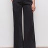 A person stands against a white wall wearing Sanctuary Clothing's cruiser full length black trousers with front patch pockets and black heeled sandals, hands in pockets, lower body only visible.
