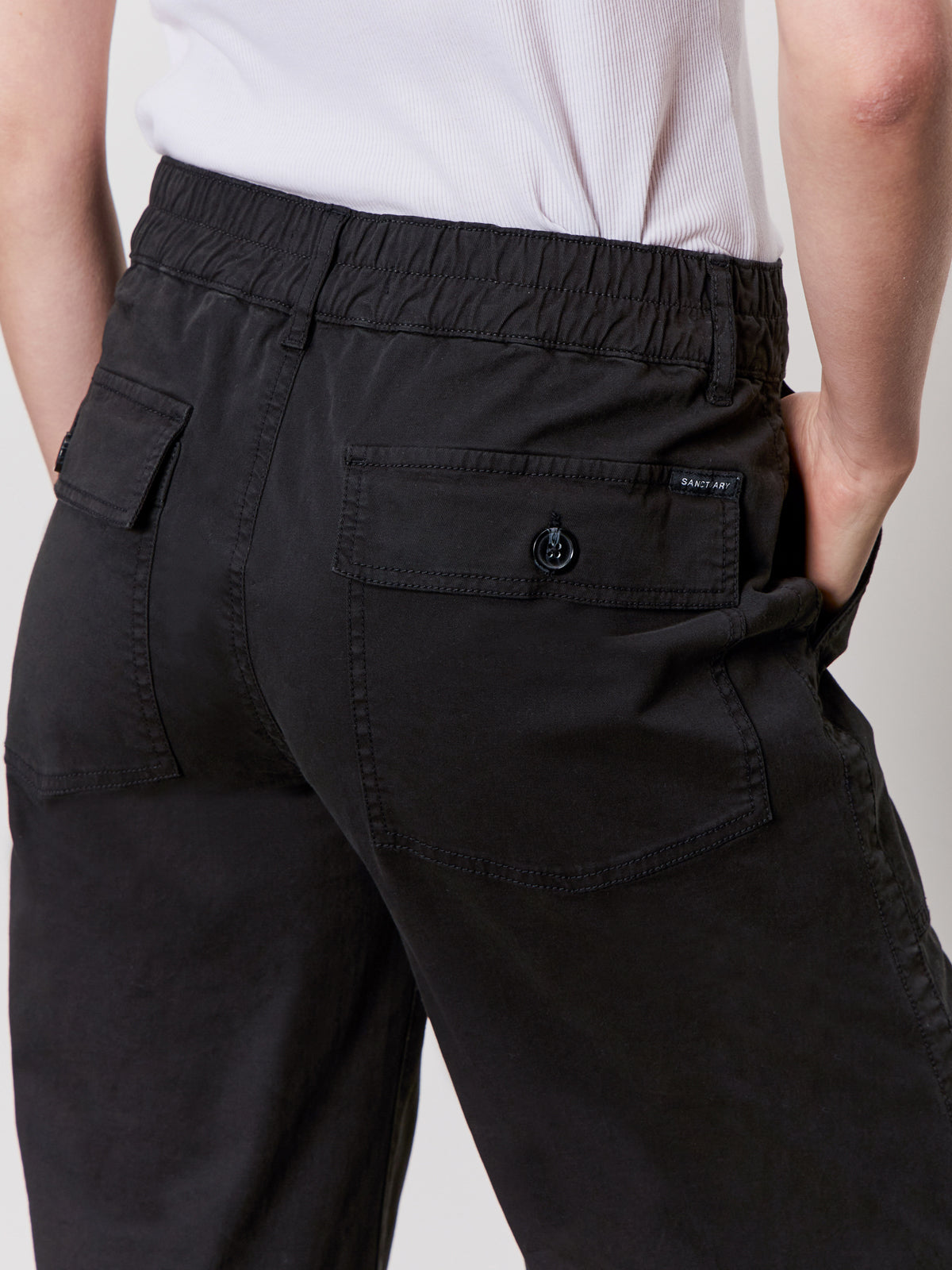 Someone wearing Sanctuary Clothing’s cruiser full length black pants with relaxed fit and flap back pockets, paired with a tucked-in white top, shown waist down from behind.