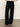 A person stands on a smooth floor wearing Sanctuary Clothing's casual track pant in black chalk stripe and black heeled sandals. The upper body is mostly out of frame, with a plain, light-colored background.