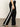 A person wearing Sanctuary Clothing's casual track pant black chalk stripe, paired with a white top and black heeled sandals, stands on a smooth brown floor against a light wall. The side view image shows them from shoulder to foot.