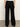 A person wearing Sanctuary Clothing’s casual track pant in black chalk stripe, featuring an elastic waistband and loose fit, is viewed from the back while standing on a smooth floor against a plain light-colored wall.