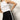 A woman models Sanctuary Clothing’s casual track pant in black with a white chalk stripe, pairing it with a sleeveless white tank top and posing against a plain light background, one hand on her hip and her head partially out of frame.