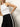 A woman models Sanctuary Clothing’s casual track pant in black with a white chalk stripe, pairing it with a sleeveless white tank top and posing against a plain light background, one hand on her hip and her head partially out of frame.