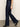 A person wearing Sanctuary Clothing's denim stunner jean plot twist and black heeled shoes walks indoors on a gray floor, with only the lower half of their body visible against a plain light-colored wall.