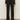 A person wears Sanctuary Clothing's the stunner pant luster stripe€�a black, high-waisted, straight-leg pant with subtle glittery pinstripes€�paired with a sheer black top and black shoes, standing against a plain light background.
