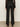 A person stands with their back turned, wearing Sanctuary Clothing's the stunner pant luster stripe€�black high-waisted pants with vertical white pinstripes€�paired with a sheer black top and black shoes against a plain background.