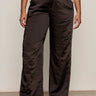 A person wearing Sanctuary Clothing's modern satin trouser in black (extended sizing), paired with a white button-up shirt and black pointed-toe heels, stands against a plain background.