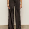 Someone wearing the Sanctuary Clothing modern satin trouser in black, styled with black pointed-toe shoes, stands against a light-colored wall on a neutral floor.