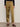 A person stands against a plain light wall wearing Sanctuary Clothing's sahara satin tapered pant in dirty martini, paired with a long-sleeve black top and brown leopard-print shoes. The photo is cropped at the shoulders.