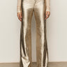 A person wearing Sanctuary Clothing's cadence relaxed straight pant in platinum, paired with a sheer long-sleeve lace top and light shoes, stands against a neutral background.