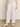 A person stands in a neutral-toned room, wearing Sanctuary Clothing's relaxed linen cruiser semi-high rise pant in bleached white and beige woven slip-on shoes. The pants are sleeveless and have a relaxed fit with front pockets, but only the lower half is visible.