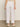 A person is seen from the rear wearing Sanctuary Clothing's relaxed linen cruiser semi high rise pant in bleached white, styled with a light crochet top and woven slip-on shoes, set against a neutral indoor background.