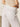 A person is wearing relaxed linen cruiser semi high-rise pants in bleached white by Sanctuary Clothing and a beige, textured, sleeveless top. The image highlights their lower back, showcasing the casual and relaxed style.