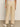 The image shows a person from the back wearing Sanctuary Clothing's relaxed linen cruiser semi high rise pants in sandstone, featuring two front pockets and two flap pockets on the back. They pair these with white sneakers and a light top, standing on a neutral-colored floor.