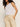 Someone with curly hair is wearing a white sleeveless top and Sanctuary Clothing's relaxed linen cruiser semi high rise pant in sandstone. Their hands are in their pants pockets as they stand against a plain background.