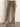 A person wears the Sanctuary Clothing cadence relaxed straight jean in light bronze with light-colored heeled shoes, standing against a plain light wall. Only the lower body is visible.