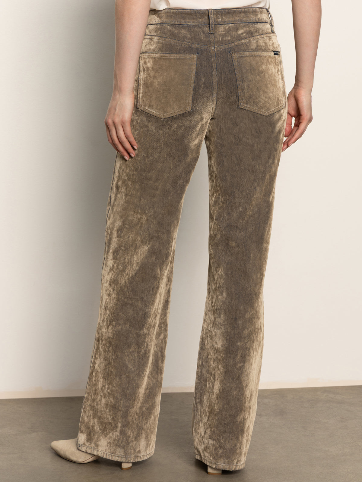 A person stands with their back to the camera, wearing Sanctuary Clothing's cadence relaxed straight jean in light bronze, paired with beige heeled shoes against a plain background.
