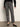 A person stands against a plain wall wearing Sanctuary Clothingžs 90s straight legging burnt olive plaid petites, paired with a black sweater and black ballet flats. Their head is out of frame.