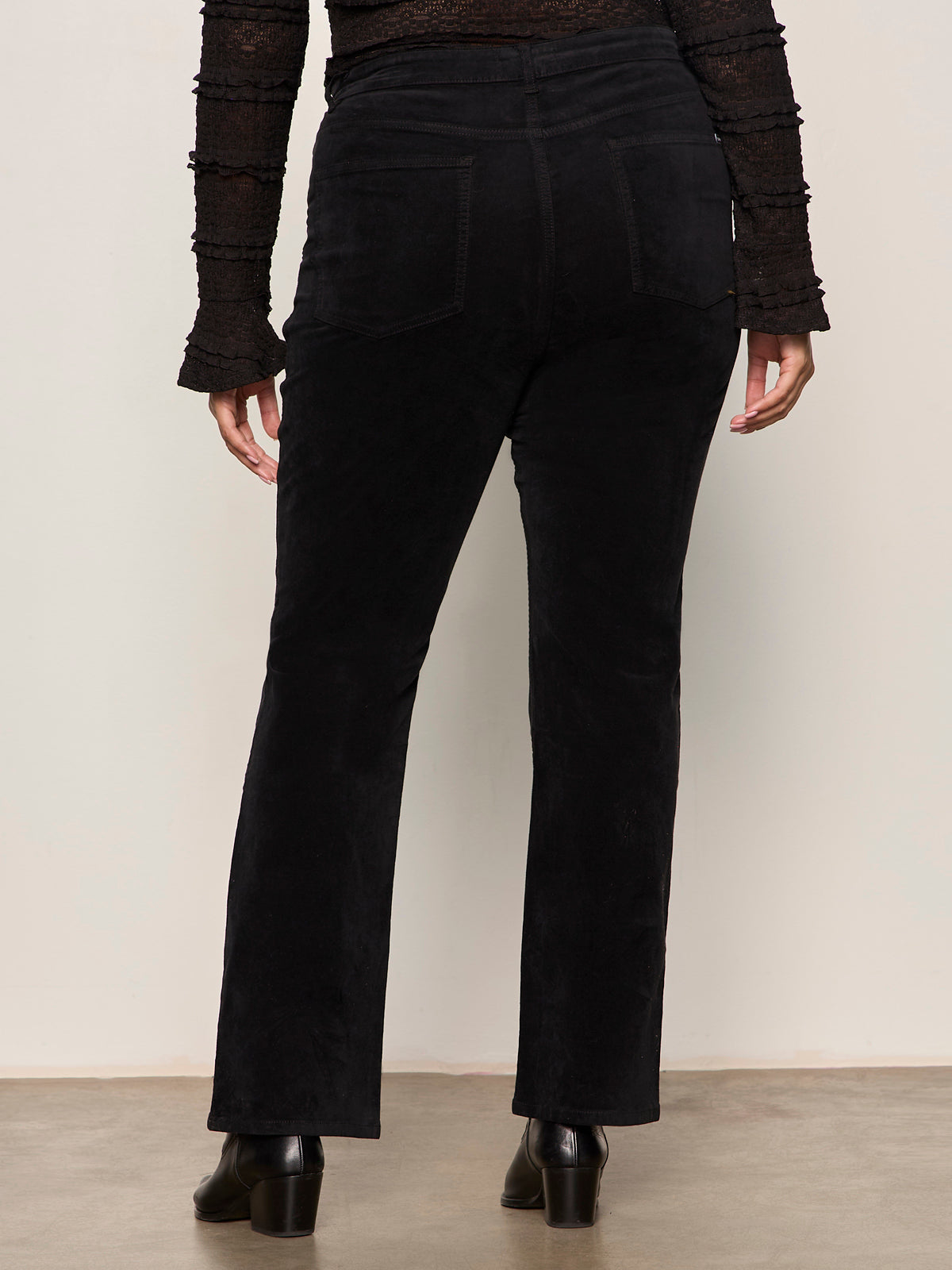 Person wearing black pants and a textured top against a plain background