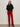 A woman with long brown hair poses against a light wall, wearing Sanctuary Clothing„¢s velveteen brook bootcut pant in cherry lacquer (petite), a black lace blouse, black belt, and black heeled ankle boots, hands in her pockets.