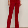 A person wears Sanctuary Clothing's velveteen brook bootcut pant in cherry lacquer (petite), styled with a black long-sleeve top and black heeled ankle boots, standing against a neutral background.