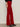 A person wearing Sanctuary Clothing„¢s velveteen brook bootcut pant in cherry lacquer (petite sizing) and black pointed-toe heeled boots stands against a neutral background with their left arm relaxed by their side.