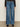 A person wears the Sanctuary Clothing tuxedo relaxed straight jean flirt€�high-waisted, wide-leg blue jeans with a dark denim side panel€�paired with a black long-sleeve top and black shoes, standing against a neutral background.