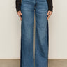 A person wears the Sanctuary Clothing tuxedo relaxed straight jean flirt€�high-waisted, wide-leg blue jeans with a dark denim side panel€�paired with a black long-sleeve top and black shoes, standing against a neutral background.