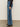 A person wearing Sanctuary Clothing's tuxedo relaxed straight jean flirt, a black long-sleeve top, and black heeled boots stands on a gray floor against a light background.