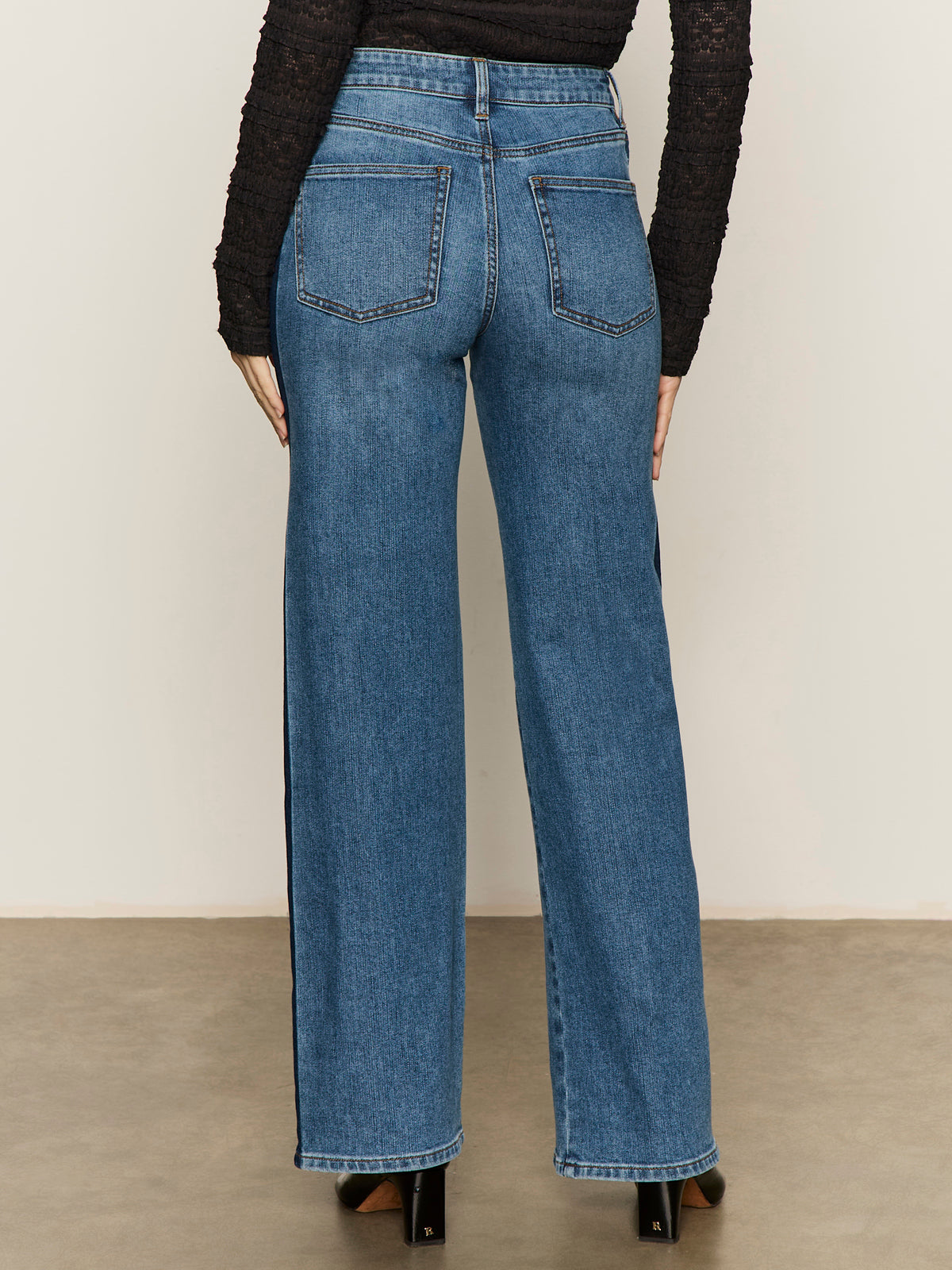 A person stands on a neutral background facing away, showcasing the back pockets of the Sanctuary Clothing tuxedo relaxed straight jean flirt paired with a long-sleeve black top.